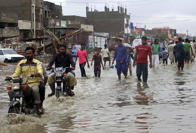 People wade through a flooded street after a heavy rainfall in Karachi, Pakistan, Tuesday, July 30, 2019. The Pakistan Meteorological Department said that a rain system entered Sindh province from India's Rajasthan and forecasts another three days of rain. (Photo by Fareed Khan/AP Photo)