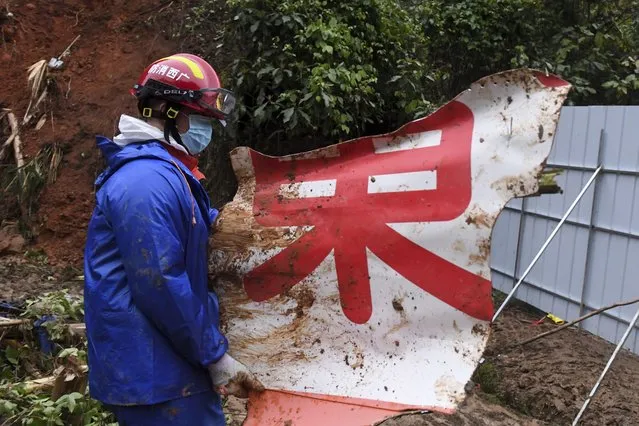 In this photo released by Xinhua News Agency, a rescue team member carries a piece of debris at the China Eastern flight crash site in Tengxian County in southern China's Guangxi Zhuang Autonomous Region on Thursday, March 24, 2022. Hundreds of people in rain gear and rubber boots searched muddy, forested hills in southern China on Thursday for the second flight recorder from a jetliner that crashed with 132 people aboard. (Photo by Lu Boan/Xinhua via AP Photo)