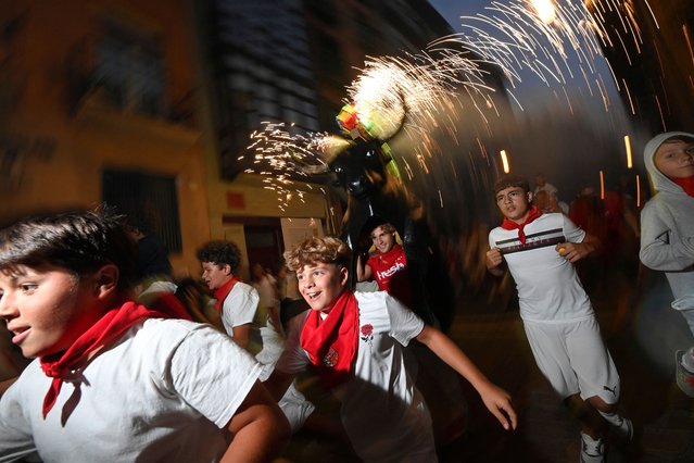 Kids run ahead of a person incarnating a “Toro de Fuego” (bull of fire) during the San Fermin Festival on July 13, 2024, in Pamplona, northern Spain. The “Toro de Fuego” (bull of fire) is a bull-shaped figure loaded with fireworks, which is carried through the streets during some festivals in Spain. The ignited fireworks create a pyrotechnic display that makes spectators run to avoid the sparks. (Photo by Miguel Riopa/AFP Photo)