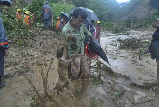 A man carries the carcass of a goat as rescuers search amid the mud after a landslide in Bandarban, Bangladesh, Tuesday, June 13, 2017. Heavy rains triggered landslides that killed dozens in southeast Bangladesh, officials said Tuesday, as police and soldiers struggled to reach the remote districts with aid. (Photo by AP Photo)