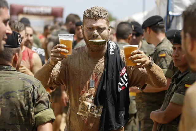 A participant with a slice of melon in his mouth carries two beers after crossing the finish line at the Mud Day athletic event at El Goloso Military base on the outskirts of Madrid, Spain, Saturday, June 11, 2016. (Photo by Paul White/AP Photo)