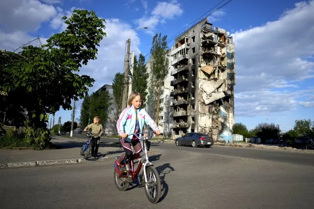 A girl rides a bicycle in front of houses ruined by shelling in Borodyanka, Ukraine, Tuesday, May 24, 2022. (Photo by Natacha Pisarenko/AP Photo)