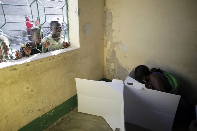 A woman casts her vote as children peek through a window at a polling station in Port-au-Prince, Haiti, August 9, 2015. (Photo by Andres Martinez Casares/Reuters)