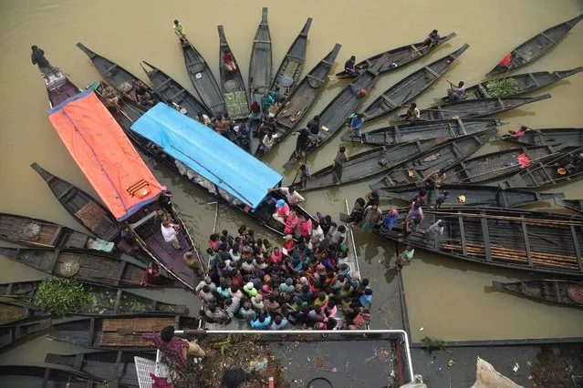 People gather to collect food aid in a flooded area following heavy monsoon rainfalls in Companiganj on June 20, 2022. (Photo by Maruf Rahman/AFP Photo)