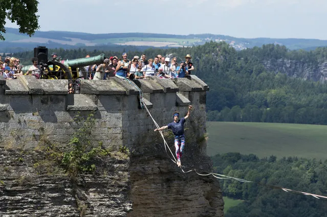 The slack line performer, Kai G., walking with along the slack rope  240 meters  above the ground outside the fortress walls of the Koengistein Fortress at river Elbe, during an outdoor sports festival in Koenigstein, eastern Germany, Saturday, August 5, 2017. (Photo by Arno Burgi/DPA via AP Photo)