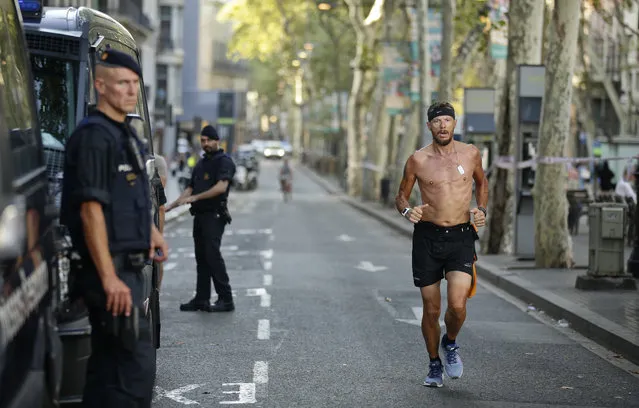 A man jogs by armed police officers standing next to their vans on a street in Las Ramblas, Barcelona, Spain, Friday, August 18, 2017. Spanish police on Friday shot and killed five people carrying bomb belts who were connected to the Barcelona van attack that killed at least 13, as the manhunt intensified for the perpetrators of Europe's latest rampage claimed by the Islamic State group. (Photo by Manu Fernandez/AP Photo)