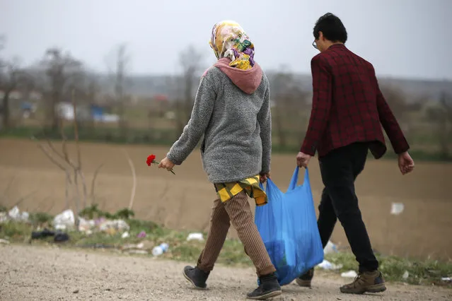 A migrant woman walks holding a carnation in Edirne near the Turkish-Greek border on Sunday, March 8, 2020. Thousands of migrants headed for Turkey's land border with Greece after President Recep Tayyip Erdogan's government said last week that it would no longer prevent migrants and refugees from crossing over to European Union territory. (Photo by Emrah Gurel/AP Photo)