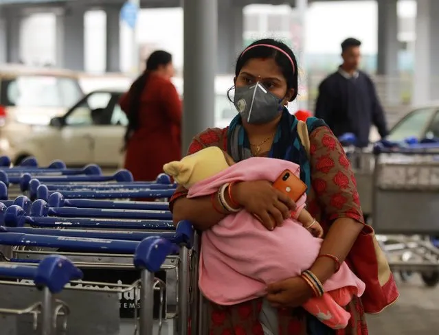 A passenger wearing a protective mask holds a baby as she waits outside an airport following an outbreak of the coronavirus disease (COVID-19), in New Delhi, India, March 14, 2020. (Photo by Anushree Fadnavis/Reuters)