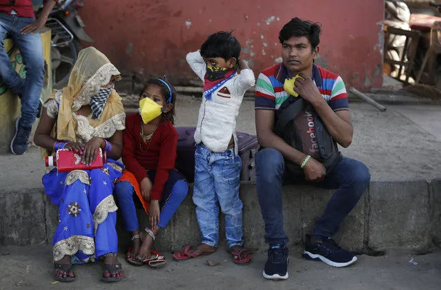 Migrant daily wage laborer Ram Bhajan Nisar and his family wait for transportation to travel to their hometown following a lockdown amid concern over spread of coronavirus in New Delhi, India, Friday, March 27, 2020. Some of India's legions of poor and others suddenly thrown out of work by a nationwide stay-at-home order began receiving aid on Thursday, as both public and private groups worked to blunt the impact of efforts to curb the coronavirus pandemic. The measures that went into effect Wednesday, the largest of their kind in the world, risk heaping further hardship on the quarter of the population who live below the poverty line and the 1.8 million who are homeless. (Photo by Manish Swarup/AP Photo)