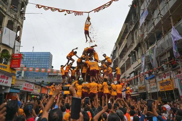 A young Hindu devotee hangs to a rope after breaking a dahi-handi (curd-pot) suspended in the air as a human pyramid collapses beneath him during celebrations for the 'Janmashtami' festival, which marks the birth of Hindu god lord Krishna, in Mumbai on August 19, 2022. (Photo by Punit Paranjpe/AFP Photo)