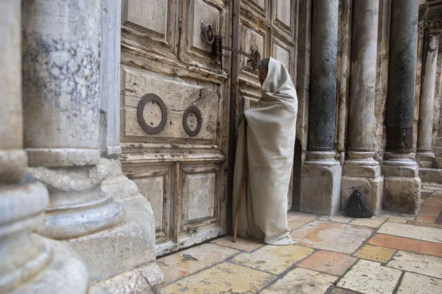 A Christian worshiper stands at the closed door of the Church of the Holy Sepulchre, believed by many Christians to be the site of the crucifixion and burial of Jesus Christ, in Jerusalem, Friday, April 10, 2020. Christians are commemorating Jesus' crucifixion without the solemn church services or emotional processions of past years, marking Good Friday in a world locked down by the coronavirus pandemic. (Photo by Sebastian Scheiner/AP Photo)