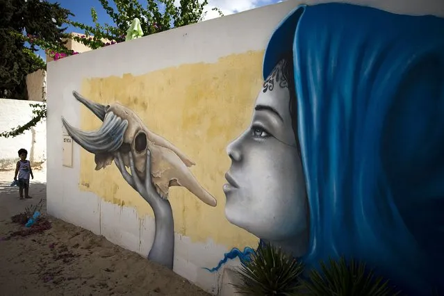 A child stands by a mural by French artist LILIWENN which decorates a wall in the village of Erriadh, on the Tunisian island of Djerba, on August 8, 2014, as part of the artistic project “Djerbahood”. (Photo by Joel Saget/AFP Photo)