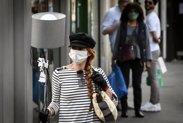 A woman wearing a face mask walks with a lamp in a street of Paris on April 25, 2020 the 40th day of a strict lockdown aimed at curbing the spread of the COVID-19 pandemic, caused by the novel coronavirus. (Photo by Alain Jocard/AFP Photo)