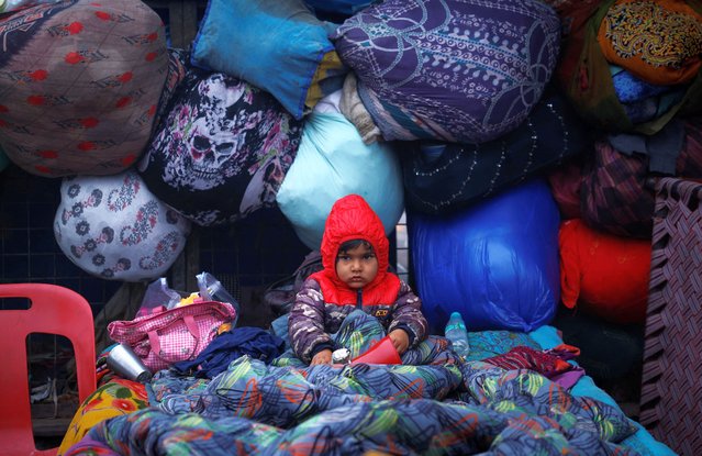 A boy wrapped in a quilt sits on a cot at a parking area on a cold winter morning in the old quarters of Delhi, India, on January 3, 2025. (Photo by Adnan Abidi/Reuters)