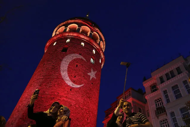 People take photos with their phones at the iconic Galata Tower, illuminated in Turkish flag colors, in Istanbul, Saturday, July 30, 2016. Dozens of staff at Turkey's highest court have been suspended from their jobs as part of the crackdown in the wake of a failed military coup, authorities said. (Photo by Petros Karadjias/AP Photo)
