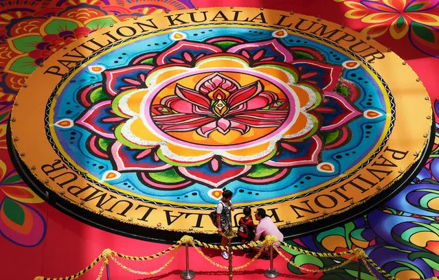 A family looks at an area decorated as a “Unity Kolam”, made of turmeric powder, rice grains and rice flour, on the floor of a shopping mall and created and displayed in conjunction with the Deepavali Hindu Festival, in Kuala Lumpur, Malaysia, 18 October 2017. The “Unity Kolam” was designed by some 100 international students from Limkokwing University, from 18 countries including Venezuela, Brazil and Maldives. The kolam design features the elephant, peacock and lotus, symbolizing power, beauty and health. (Photo by Fazry Ismail/EPA/EFE)
