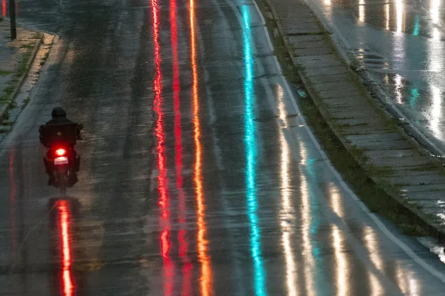 A delivery motorcyclist rides in a rain storm through what is normally one of the busiest intersection during rush hour in Johannesburg's northern suburbs Tuesday, April 14, 2020 downtown Johannesburg. South Africa is under a strict five-week lockdown credited with slowing the rate of COVID-19 infections and reducing overall crime. (Photo by Jerome Delay/AP Photo)