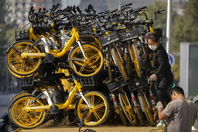 A worker wearing a face mask walks along a trailer full of rental bicycles parked along a street in Beijing, Wednesday, October 19, 2022. (Photo by Mark Schiefelbein/AP Photo)