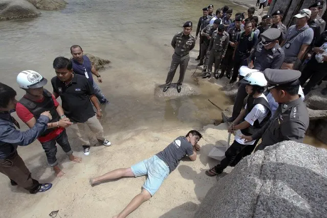 Two workers from Myanmar (wearing helmets and handcuffs), suspected of killing two British tourists on the island of Koh Tao last month, stand near Thai police officers during a re-enactment of the alleged crime, where the bodies of the tourists were found on the island October 3, 2014. (Photo by Reuters/Stringer)