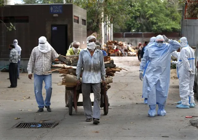 Workers push a handcart carrying wood for the funeral pyre of victims of COVID-19, at a crematorium in New Delhi, India. Friday, June 5, 2020. The coronavirus pandemic is leaving India's morgues piling up with the dead and graveyards and crematoriums overwhelmed. Like elsewhere in the world, the virus has made honoring the dead in New Delhi a hurried affair, largely devoid of the rituals that give it meaning for mourners. (Photo by Manish Swarup/AP Photo)