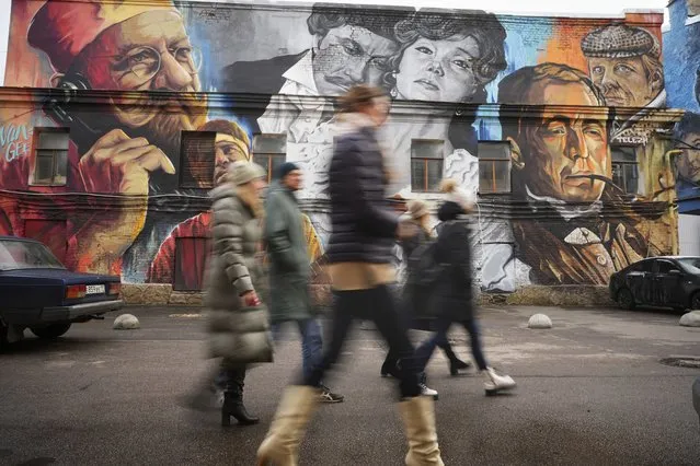 People walk past a mural depicting the characters of famous Soviet films on the building of the Lenfilm film company in St. Petersburg, Russia, Wednesday, November 16, 2022. (Photo by Dmitri Lovetsky/AP Photo)