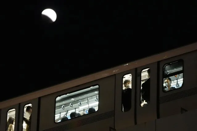People ride on a train during a lunar eclipse over the Tokyo sky on Tuesday, November 8, 2022. (Photo by Hiro Komae/AP Photo)