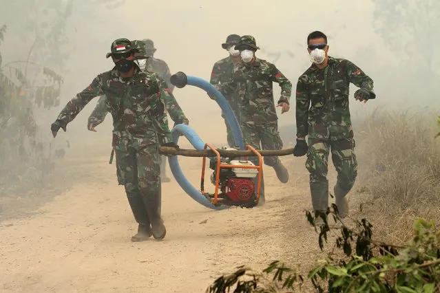 Indonesian soldiers carry a gas powered water pump used to help extinguish a peatland fire in Ogan Ilir, South Sumatra province on the island of Sumatra, September 30, 2015 in this photo taken by Antara Foto. An Indonesian government official said the country is hoping rain will help put out forest fires that have been raging for weeks in the northern islands, causing haze to blanket parts of Southeast Asia. (Photo by Nova Wahyudi/Reuters/Antara Foto)