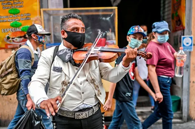 A Mariachi wears a face mask as he perform on the street to earn some money due to the lack of work amid the COVID-19 novel coronavirus pandemic, in Mexico City on August 7, 2020. Latin America and the Caribbean surpassed Europe on Friday to become the region hardest-hit by coronavirus deaths. Worldwide there have been more than 715,000 deaths from the virus first reported in China at the end of last year. (Photo by Pedro Pardo/AFP)