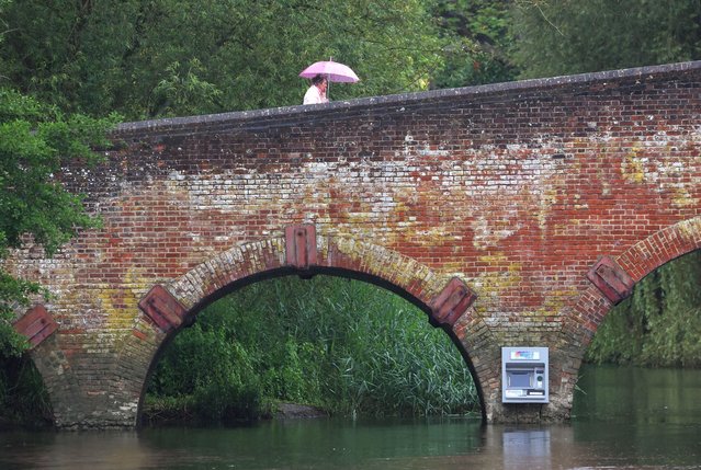 A person walks above an art installation of an ATM cashpoint attached to Sonning Bridge and attributed to the anonymous artist Impro, in Sonning, southern Britain on July 9, 2024. (Photo by Toby Melville/Reuters)