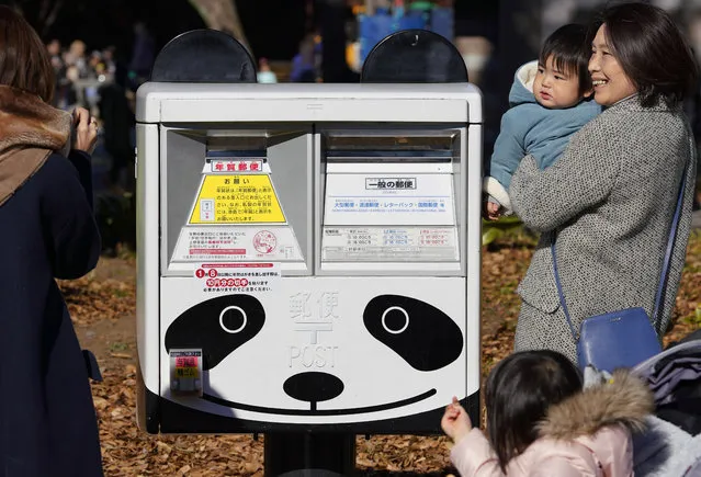 In this Sunday, December 17, 2017, photo, a family takes a photo with a mailbox featuring a giant panda near Ueno Zoo in Tokyo. Tokyo’s new idol, baby panda Xiang Xiang, formally debuted Tuesday, immediately melting the hearts of hundreds of fans decorating themselves with panda motifs who visited the zoo and the neighborhood filled with festivity. (Photo by Shizuo Kambayashi/AP Photo)