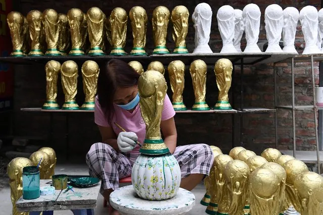 A worker paints a plaster model of the FIFA World Cup trophy at a workshop in Hanoi on November 16, 2022, ahead of the Qatar 2022 World Cup football tournament. (Photo by Nhac Nguyen/AFP Photo)