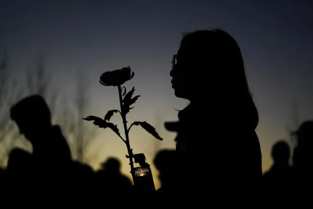 A woman holds a candle and a flower during a vigil outside Monterey Park City Hall, blocks from the Star Ballroom Dance Studio, late Tuesday, January 24, 2023, in Monterey Park, Calif. A gunman killed multiple people at the ballroom dance studio late Saturday amid Lunar New Year's celebrations in the predominantly Asian American community. (Photo by Ashley Landis/AP Photo)
