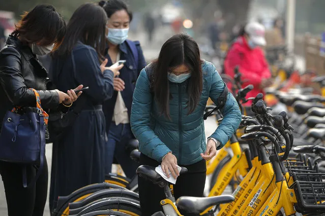 A woman wearing a face mask to help curb the spread of the coronavirus uses an alcohol tissue to disinfect a bicycle of bike-sharing companies during the morning rush hour in Beijing, Monday, October 26, 2020. Schools and kindergartens have been suspended and communities are on lockdown in Kashgar, a city in China's northwest Xinjiang region, after more than 130 asymptomatic cases of the coronavirus were discovered. (Photo by Andy Wong/AP Photo)