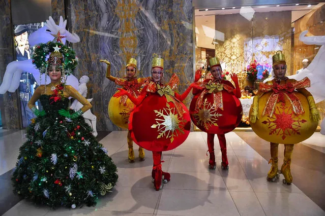 Models and dancers dressed as Christmas trees and baubles while wearing face shields put on a display for shoppers in a shopping mall in Bangkok in December 24, 2020. (Photo by Lillian Suwanrumpha/AFP Photo)