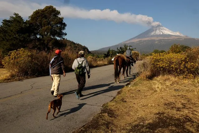 Residents walk along a road as steam and ashes emerge from the Popocatepetl volcano, after an increase in volcanic activity, as seen from the town of Santiago Xalizintla, Mexico on May 12, 2023. (Photo by Imelda Medina/Reuters)