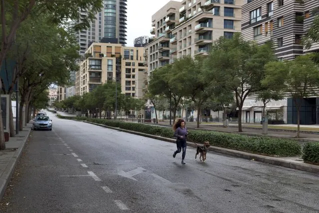 A woman runs with her dog in an almost empty street during a lockdown aimed at curbing the spread of the coronavirus, in Beirut, Lebanon, Thursday, January 14, 2021. Lebanese authorities began enforcing an 11-day nationwide shutdown and round the clock curfew Thursday, hoping to limit the spread of coronavirus infections spinning out of control after the holiday period. (Photo by Bilal Hussein/AP Photo)