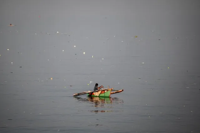 A woman fishes from a boat while trash floats in the waters of Baseco Beach on World Oceans Day, in Manila, Philippines on June 8, 2023. (Photo by Eloisa Lopez/Reuters)