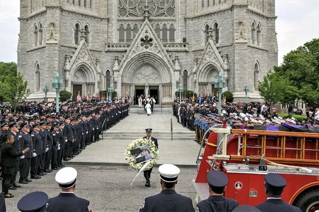 A wreath of flowers with a picture of the deceased is carried to a fire truck during the funeral service for veteran Newark Firefighter Augusto Acabou at the Cathedral Basilica of the Sacred Heart in Newark, New Jersey, USA, 13 July 2023. Wayne Brooks Jr. and Augusto Acabou died in the line of duty last week while battling the massive cargo ship fire at Port Newark. The cause of the fire and of their death remains under investigation. (Photo by Sarah Yenesel/EPA)