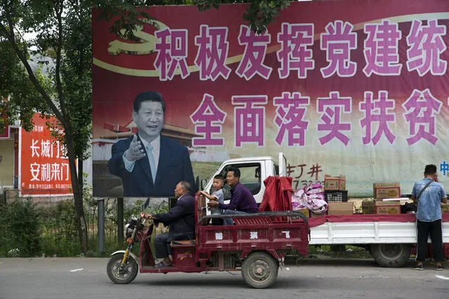 In this photo taken Saturday, June 2, 2018, residents past by a poster of Chinese President Xi Jinping and part of the slogans which reads “Actively play the leading role of party building and comprehensively implement the plan for poverty alleviation” near Pingdingshan city in central China's Henan province. Under President Xi Jinping, China's most powerful leader since Mao Zedong, believers are seeing their freedoms shrink dramatically even as the country undergoes a religious revival. Experts and activists say that as he consolidates his power, Xi is waging the most severe systematic suppression of Christianity in the country since religious freedom was written into the Chinese constitution in 1982. (Photo by Ng Han Guan/AP Photo)