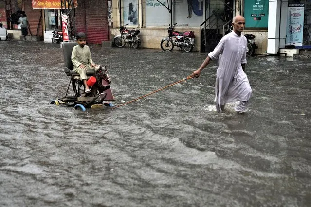 A man pulls a handcart carrying a boy as they wade through a flooded road caused by heavy monsoon rainfall in Lahore, Pakistan, Wednesday, July 5, 2023. Officials say heavy monsoon rains have lashed across Pakistan, killing a number of people. (Photo by K.M. Chaudary/AP Photo)