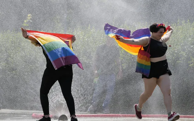 A women with a rainbow flag cools off in a sprinkler ahead of the Equality Parade, the largest LGBT pride parade in Central and Eastern Europe, in Warsaw, Poland, Saturday, June 19, 2021. (Photo by Czarek Sokolowski/AP Photo)