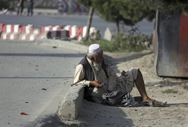 An injured civilian uses a cellphone as he sits on the ground after an attack near the Kabul Airport, in Kabul, Afghanistan, Sunday, July 22, 2018. An Afghan spokesman said there has been a large explosion near the Kabul airport shortly after the country's controversial first vice president landed on his return from abroad. Gen. Abdul Rashid Dostum and members of his entourage were unharmed in the explosion on Sunday, which took place as his convoy had already left the airport. (Photo by Rahmat Gul/AP Photo)