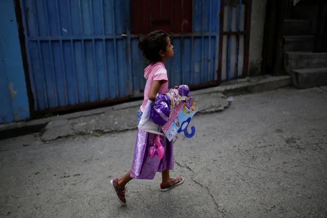A girl walks with a costume received during a toy distribution program with Miguel Pizarro, deputy of the Venezuelan coalition of opposition parties (MUD), at the slum of Petare in Caracas, Venezuela December 20, 2016. (Photo by Marco Bello/Reuters)