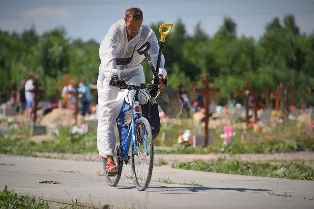A worker in a protective suit rides a bicycle after a funeral of deceased COVID-19 patients at the Novoye Kolpinskoye cemetery in St Petersburg, Russia on July 1, 2021. (Photo by Peter Kovalev/TASS)