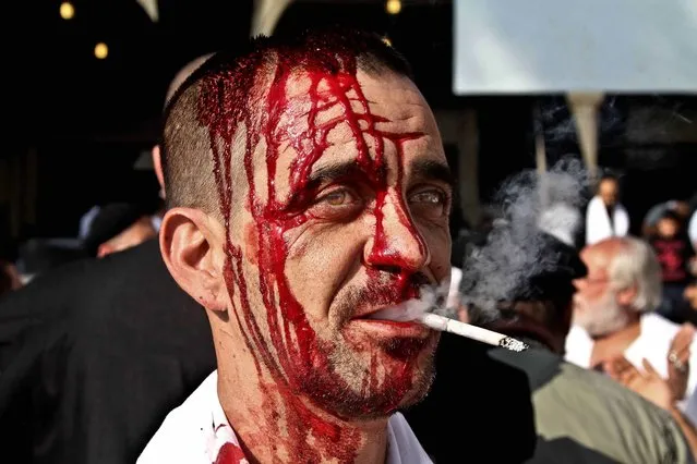 A Lebanese Shiite smokes a cigarette as he bleeds from his head from self inflicted wounds, during Ashoura in the southern market town of Nabatiyeh, Lebanon, Thursday, November 14, 2013. Thursday's commemorations marked the climax of Ashoura, the yearly mourning period in which Shiite Muslims remember the seventh century death of the Prophet Muhammad's grandson, Imam Hussein, in a battle in the central city of Karbala. (Photo by Mohammed Zaatari/AP Photo)