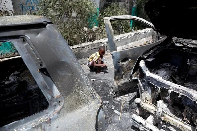 A child looks for metal pieces while sitting behind cars burnt by locals after a firefight between police and the suspected assassins of President Jovenel Moise who was shot dead early Wednesday at his home, in Port-au-Prince, Haiti on July 8, 2021. (Photo by Estailove St-Val/Reuters)