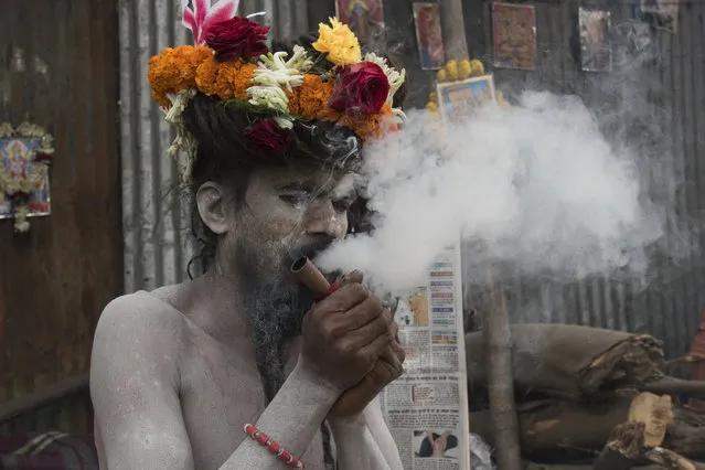 This naga sadhu adorns his jata (long tangled hair) with flowers brought by the devotees. A cloud of smoke covers him as he puffs distractedly at his chhilm. Babughat, Kolkata, India on 11 January 2017. (Photo by Sushavan Nandy/NurPhoto)