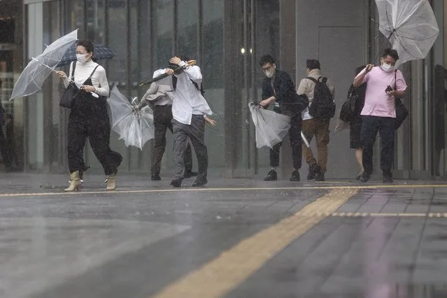 People struggle with rain and strong wind as Typhoon Mindulle travels off the coast of Japan Friday, October 1, 2021, in Tokyo. (Photo by Kiichiro Sato/AP Photo)
