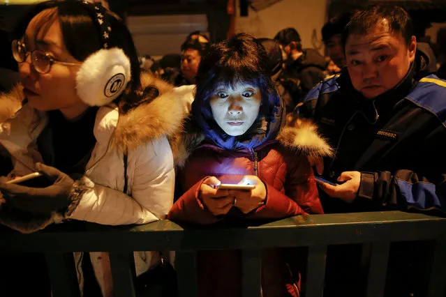 People use their phones as they wait for Yonghegong Lama Temple to open its gates so they can burn incense and pray for good fortune on the first day of the Lunar New Year of the Rooster in Beijing, China January 28, 2017. (Photo by Damir Sagolj/Reuters)
