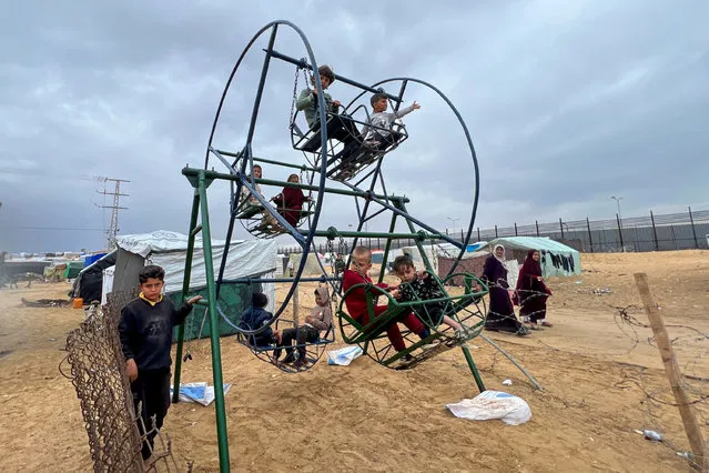 Displaced Palestinian children, who fled their houses due to Israeli strikes, amid the ongoing conflict between Israel and the Palestinian Islamist group Hamas, play on swings at a tent camp at the border with Egypt, amid fears of an Israeli ground assault in Rafah, in the southern Gaza Strip on February 18, 2024. (Photo by Saleh Salem/Reuters)